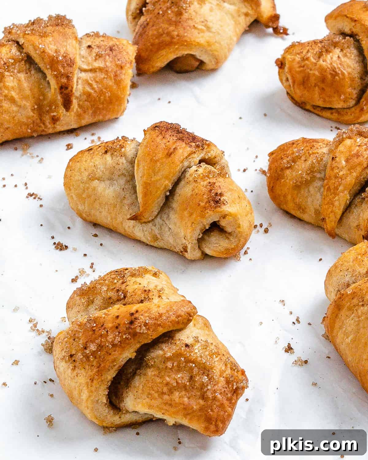 Golden Apple Cinnamon Crescents 15 A final shot of numerous perfectly baked vegan apple crescent rolls scattered appealingly on a white surface.