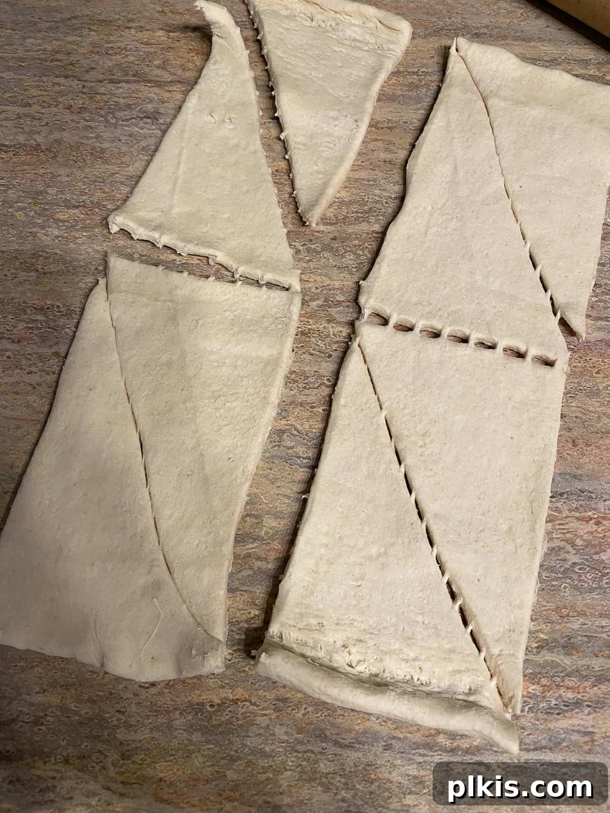 Golden Apple Cinnamon Crescents 9 Unrolled crescent roll dough triangles scattered on a brown surface, ready for filling.