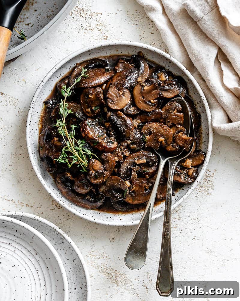 Sizzling Garlic Thyme Mushrooms 2 completed Sauteed Mushrooms with Garlic and Thyme on a white surface, garnished with fresh herbs