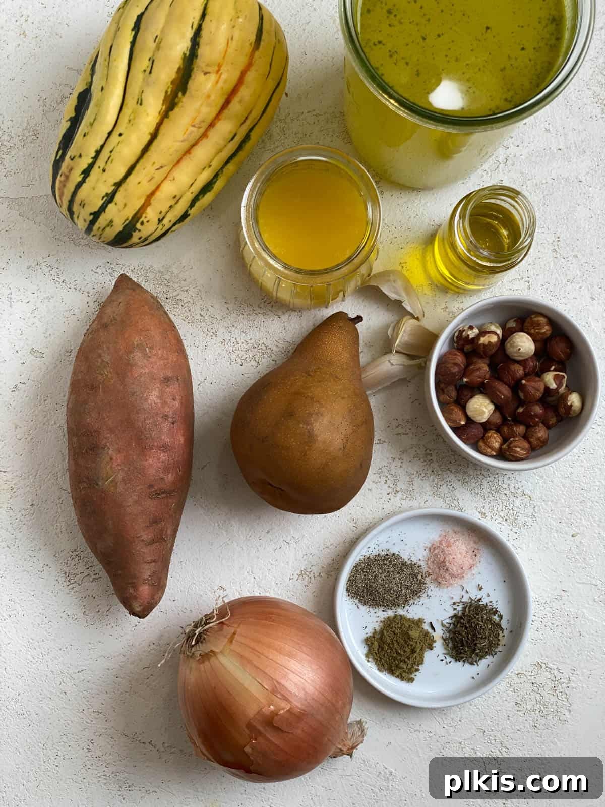 Golden Roasted Delicata Sweet Potato Soup 3 Ingredients for Roasted Delicata Squash and Sweet Potato Soup laid out on a light surface, including squash, sweet potato, pear, onion, garlic, and broth
