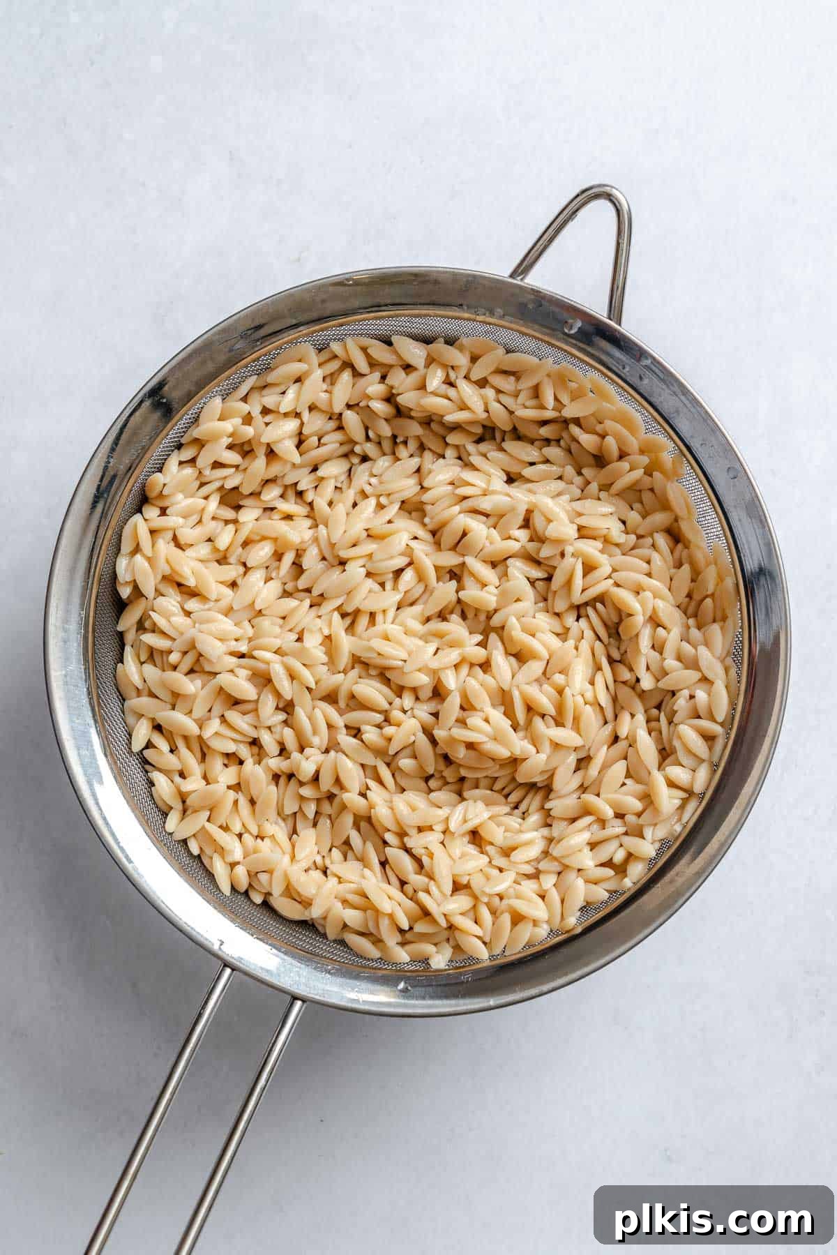 Zesty Lemon Orzo Salad 4 Process shot showing cooked orzo pasta being drained in a strainer under cold water to stop the cooking process.