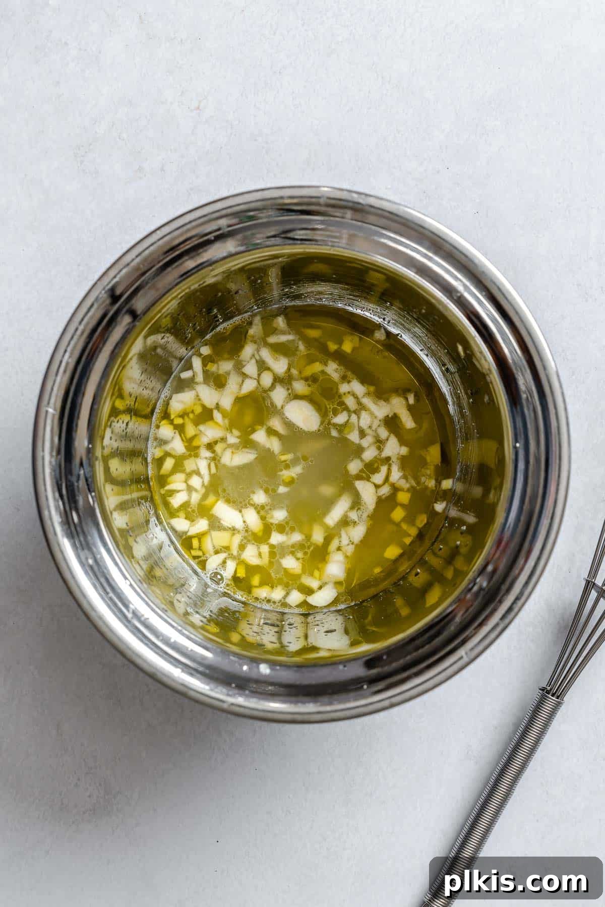 Zesty Lemon Orzo Salad 5 Process shot showing a small bowl where olive oil, lemon juice, minced garlic, and salt are being whisked together to create the salad dressing.