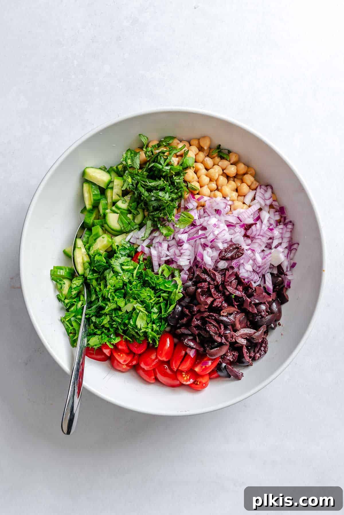 Zesty Lemon Orzo Salad 6 Process shot showing all the prepared ingredients for the Lemon Orzo Salad, including cooled orzo, sliced cucumbers, halved cherry tomatoes, drained chickpeas, diced red onion, diced Kalamata olives, and chopped fresh herbs, gathered in a large mixing bowl before dressing.