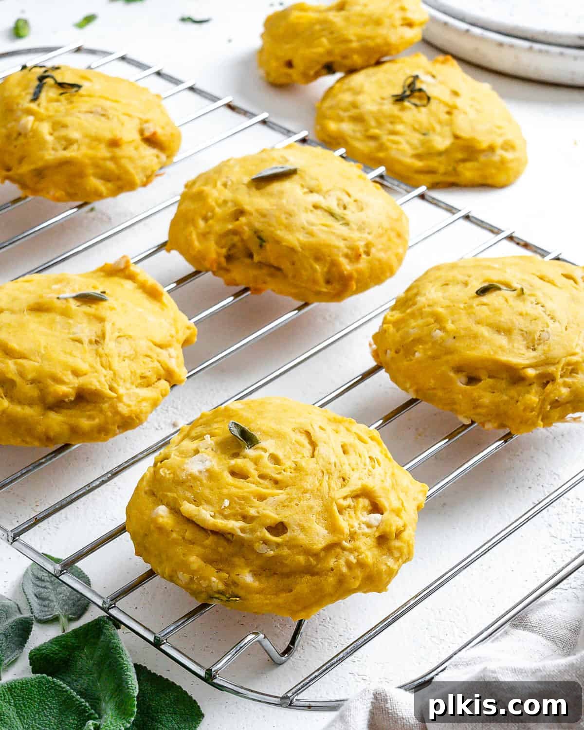 Golden Sage Butternut Biscuits 11 A close-up shot of two perfectly baked Butternut Squash Sage Biscuits, one garnished with a fresh sage leaf, on a wire rack.
