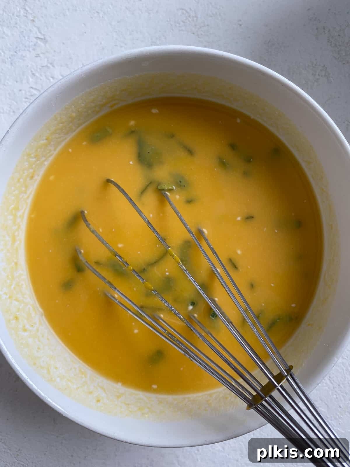 Golden Sage Butternut Biscuits 7 Butternut squash puree, plant-based milk mixture, and chopped sage being combined in a bowl with a whisk.