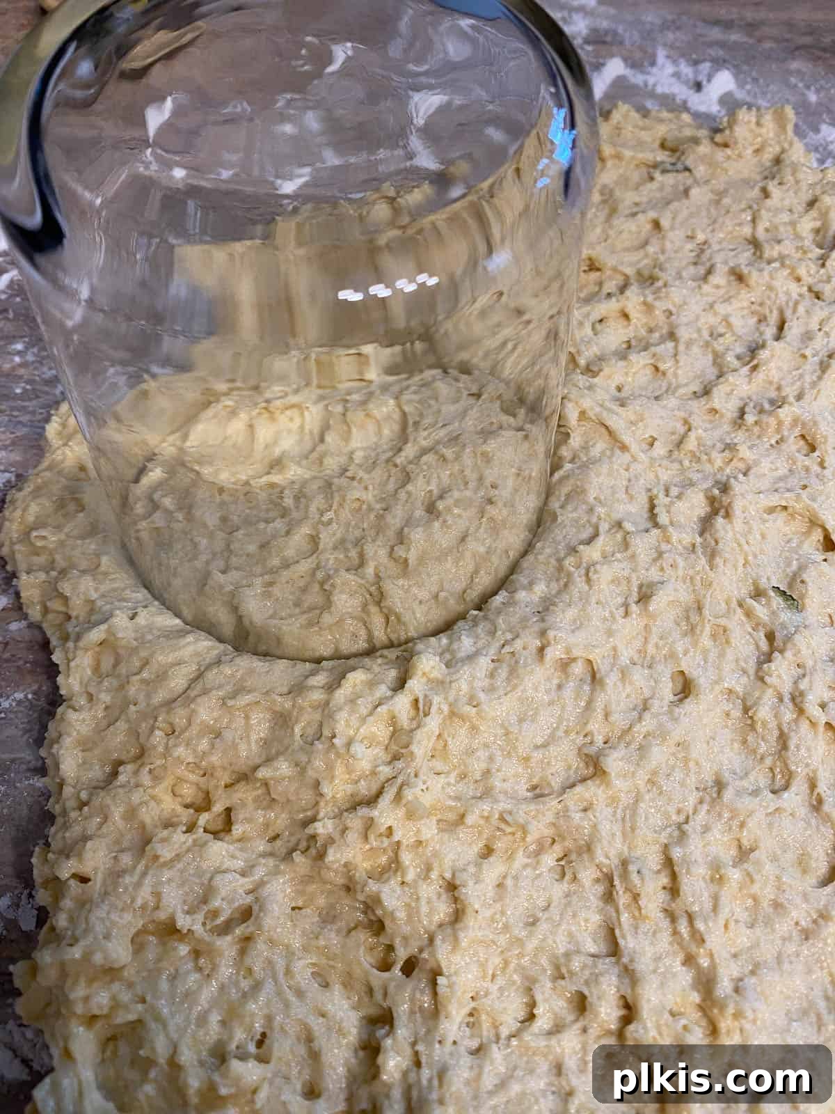 Golden Sage Butternut Biscuits 9 Biscuit dough being cut into uniform rounds using an upside-down drinking glass on a lightly floured surface.