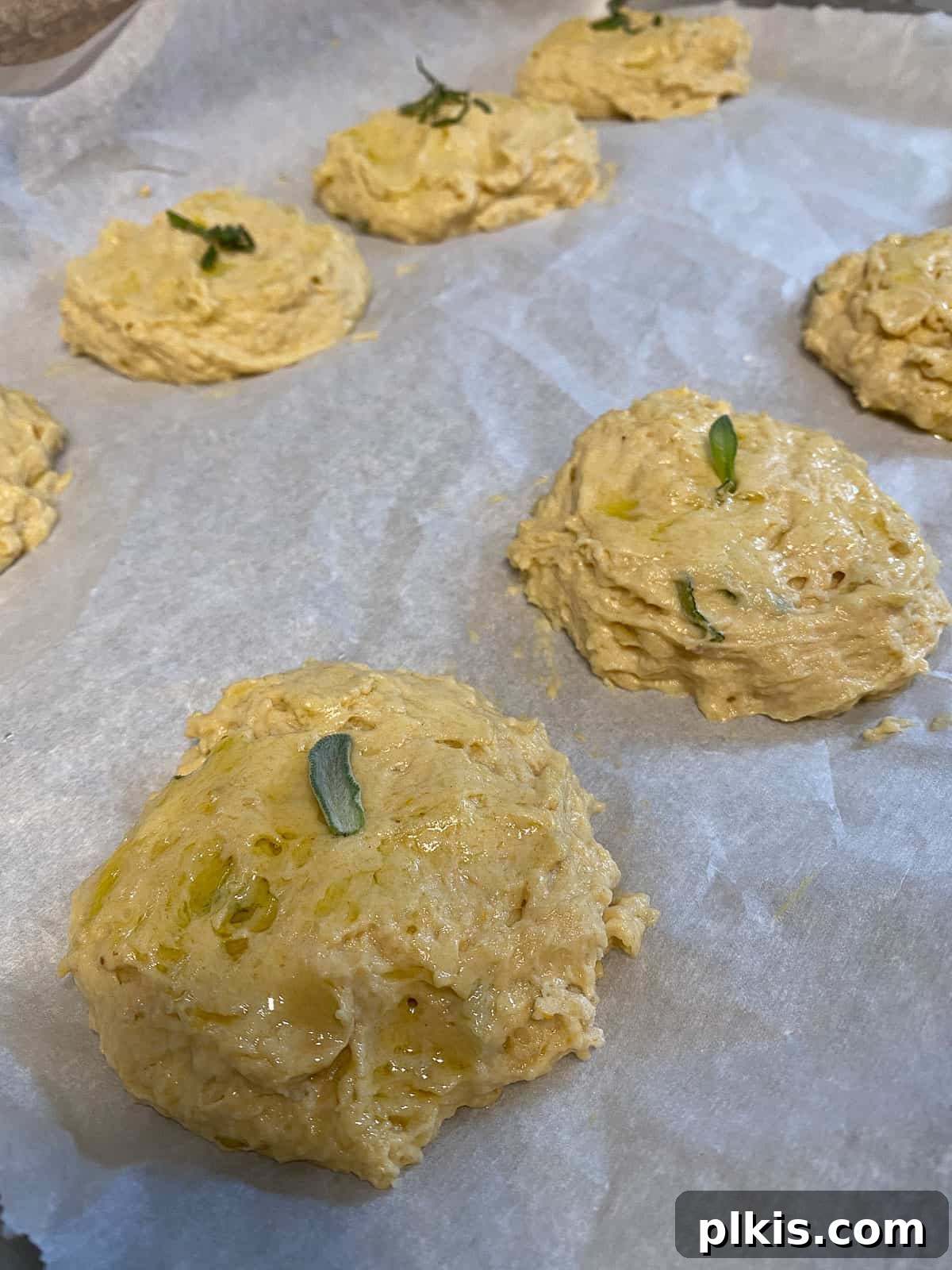 Golden Sage Butternut Biscuits 10 Butternut Squash Sage Biscuits arranged on parchment paper on a baking sheet, ready for the oven.