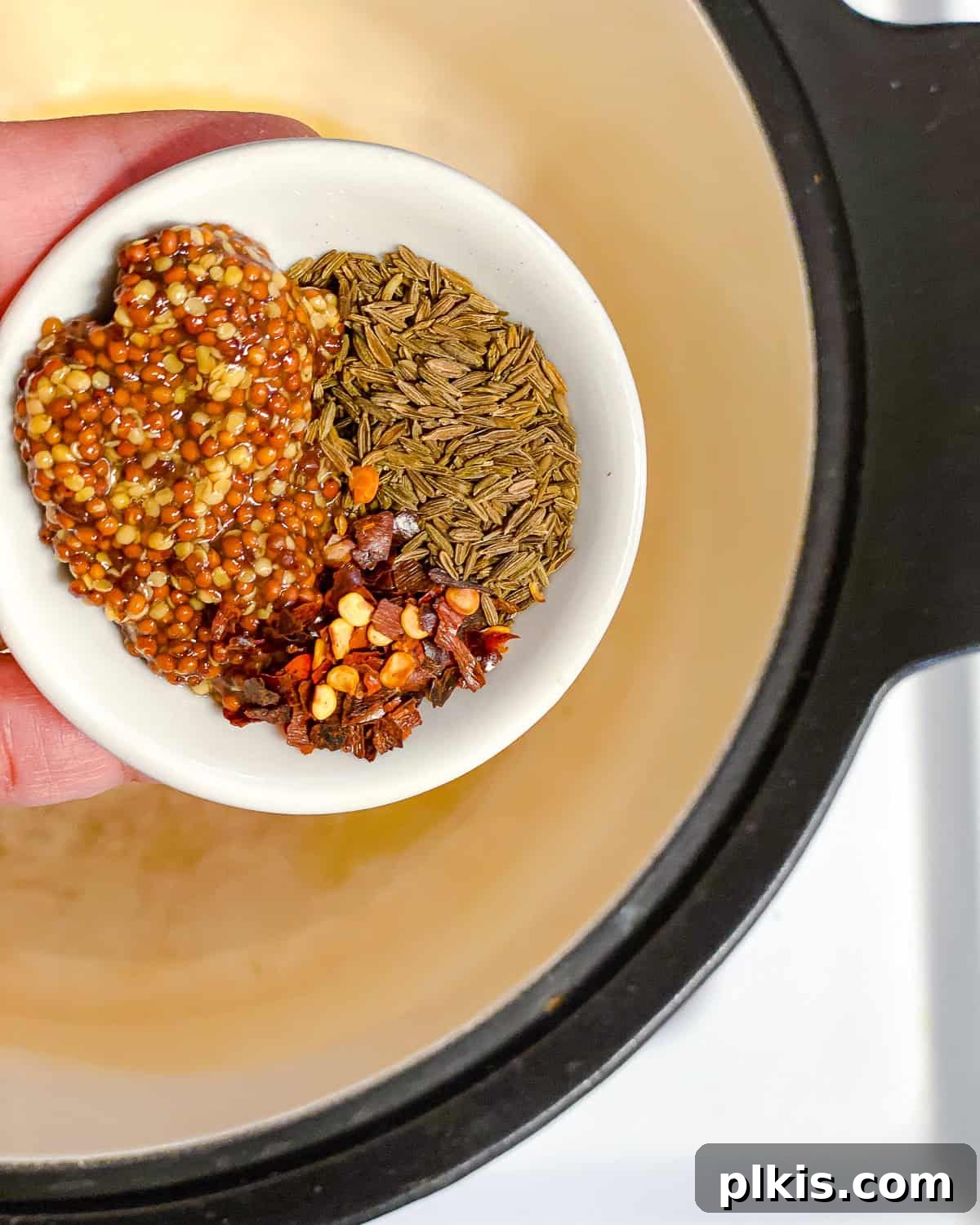 Hearty Butternut Squash and Lentil Soup 4 Process shot showing a hand adding whole spices like mustard and cumin seeds to a hot pot with oil.