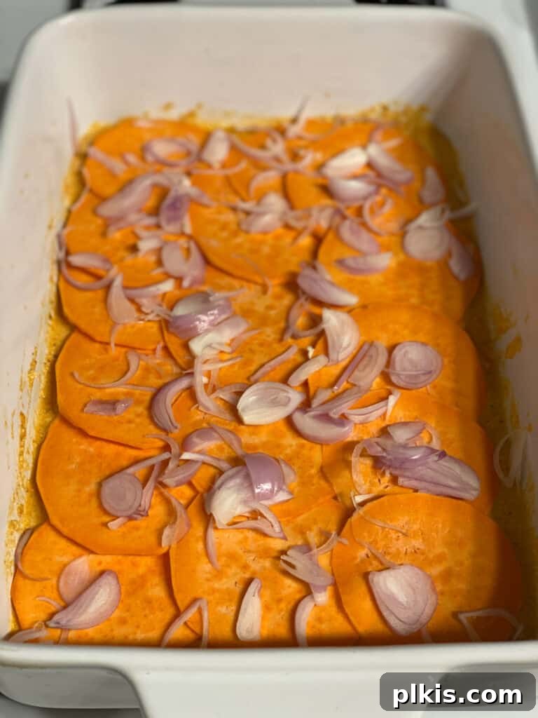 Process shot: Finely sliced shallots being sprinkled evenly over a layer of sweet potatoes in the baking dish, adding a mild onion flavor.