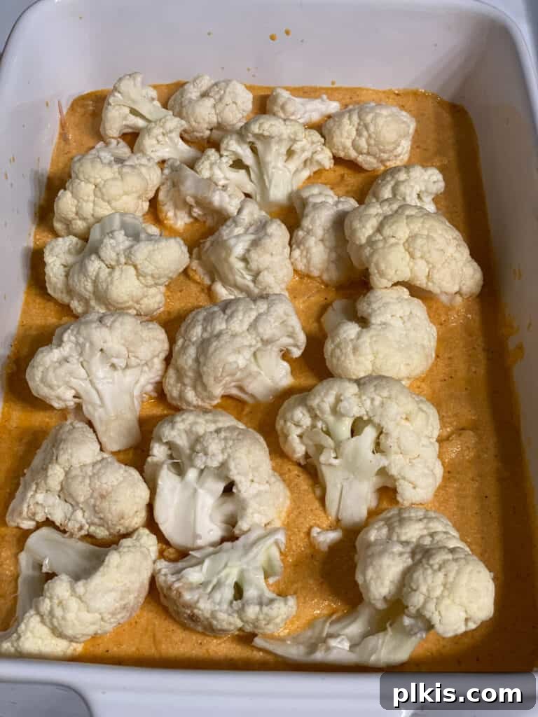 Process shot: Cauliflower florets being evenly distributed over a layer of sauce and sweet potatoes in the casserole dish.