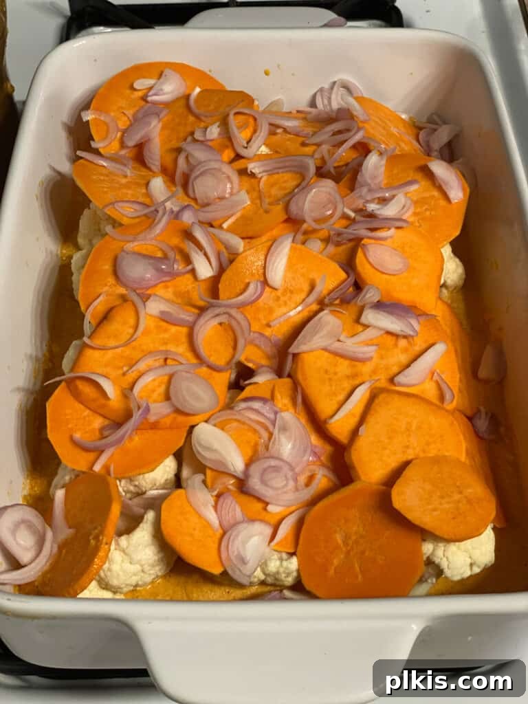 Process shot: Another layer of thinly sliced sweet potatoes and chopped shallots being added to the casserole, building up the flavorful layers.