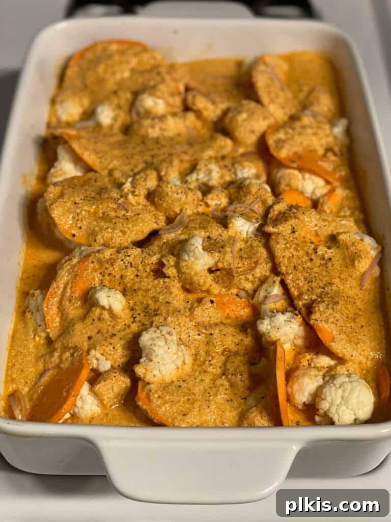 Process shot: The final layer of creamy red pepper cashew sauce being spread over the assembled casserole before baking, creating a smooth top.