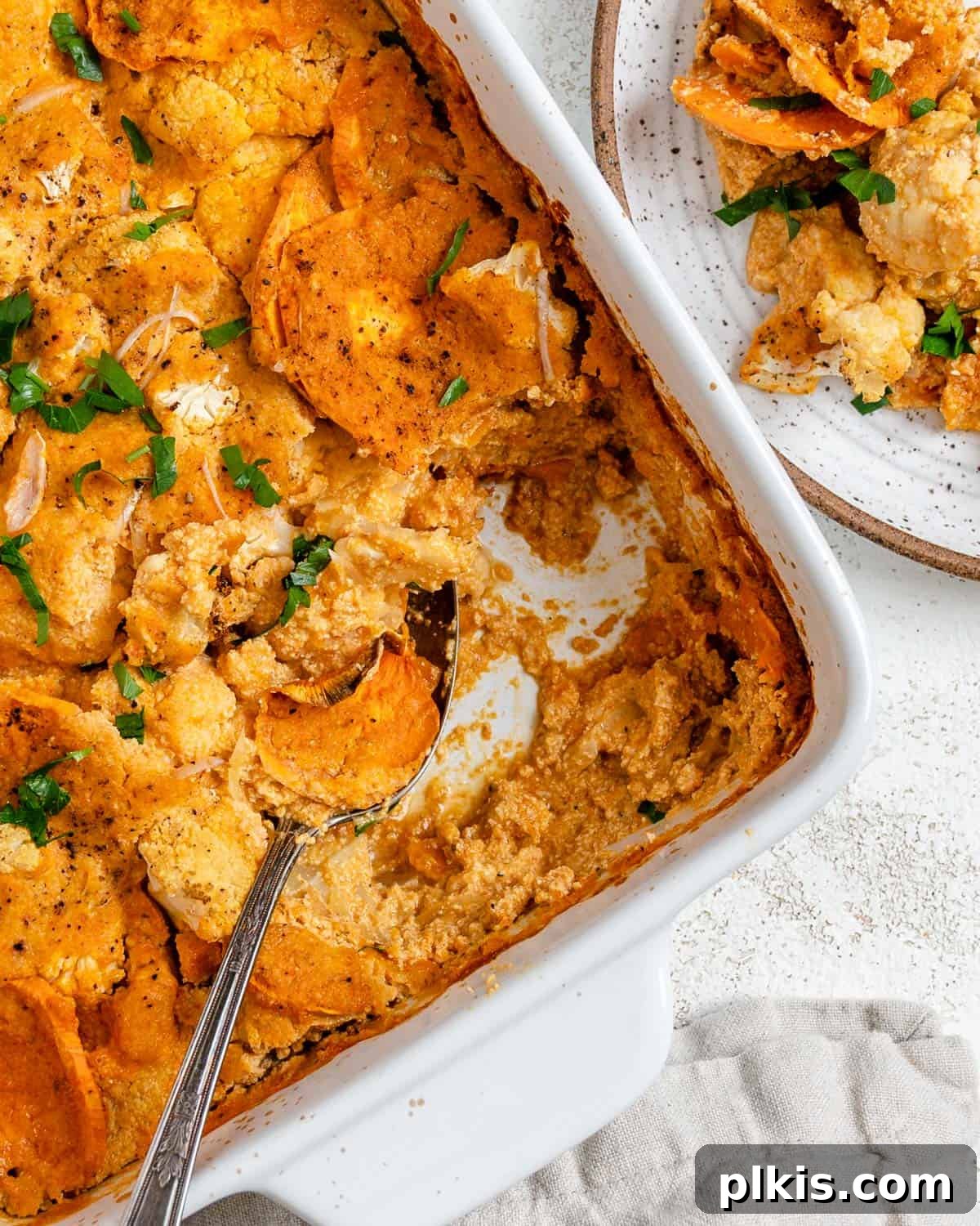 A beautifully plated slice of Healthy Vegan Cauliflower Casserole, showcasing its creamy layers and golden-brown top, garnished with fresh herbs, set against a pristine white background.