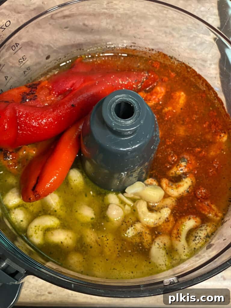 Process shot: Ingredients for the cashew cream sauce, including cashews, roasted red peppers, and spices, being added to a food processor.