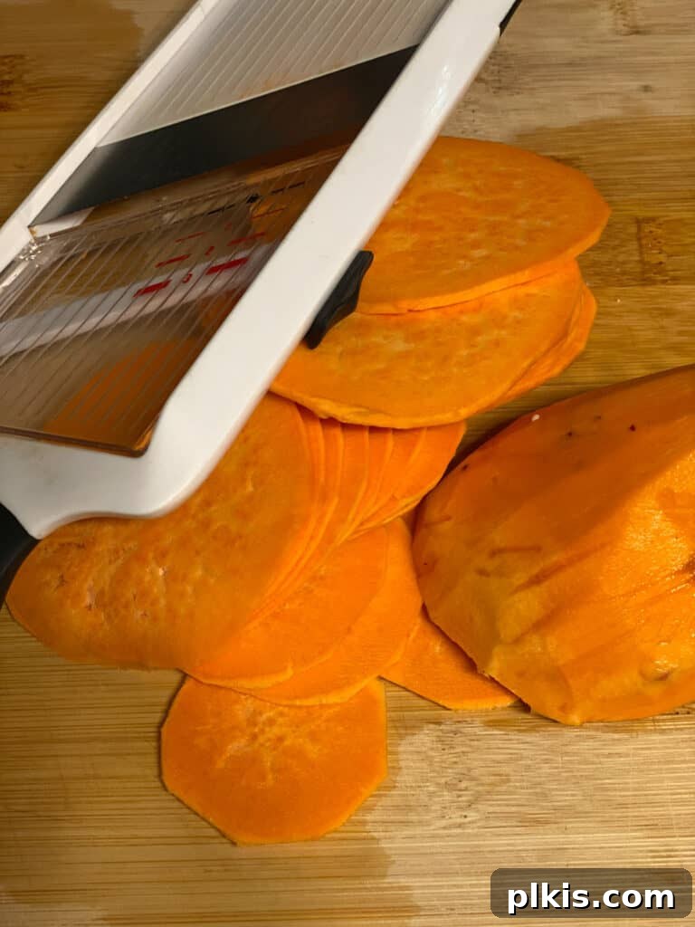 Process shot: A person expertly slicing sweet potatoes into thin, even rounds using a mandoline on a cutting board.