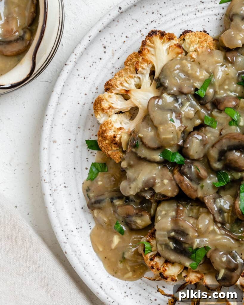 A beautifully arranged serving of cauliflower steaks with a generous drizzle of mushroom gravy on a white plate, presented as a complete meal.