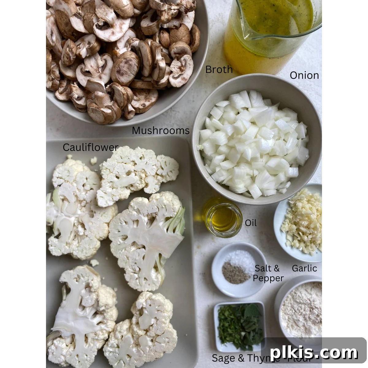 Fresh ingredients for homemade cauliflower steaks and mushroom gravy, including a whole cauliflower head, sliced mushrooms, onions, herbs, and spices, neatly arranged on a white surface.