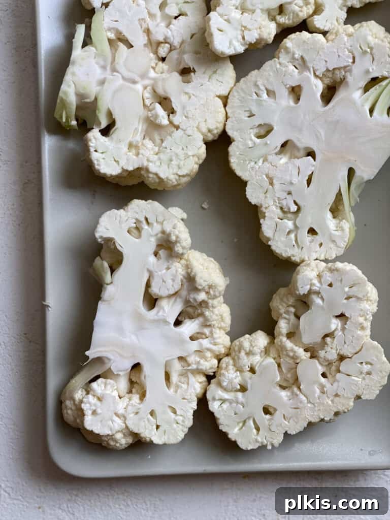 Cauliflower head sliced into thick steaks, neatly arranged on a baking sheet, ready for seasoning and cooking.