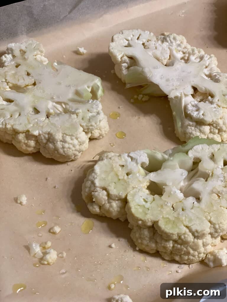 Seasoned cauliflower steaks laid out on a baking sheet, ready to be transferred to the oven for roasting.
