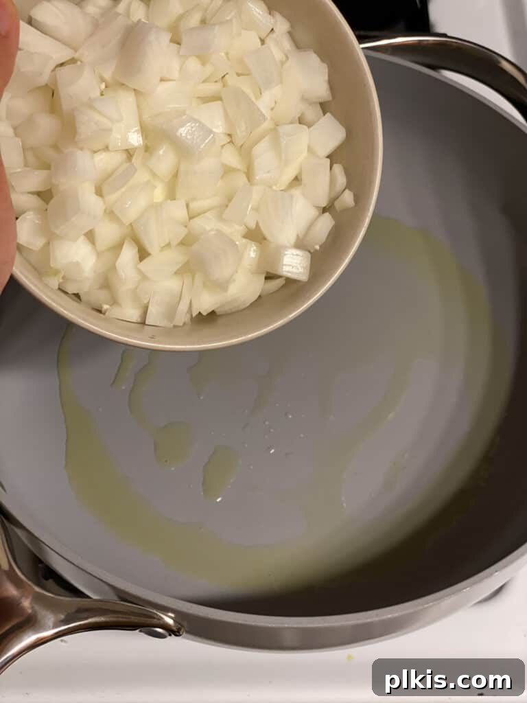 Diced yellow onion being added to a hot pan with oil, beginning the aromatic base for the mushroom gravy.