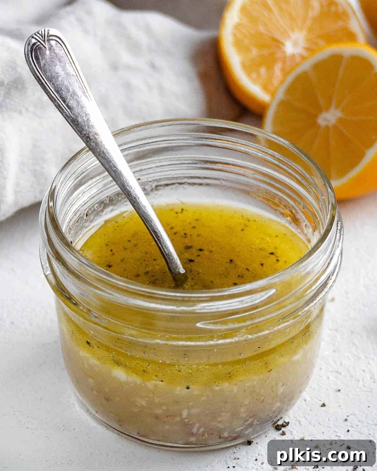 completed lemon dressing in a glass jar with a spoon in it and ingredients in the white background