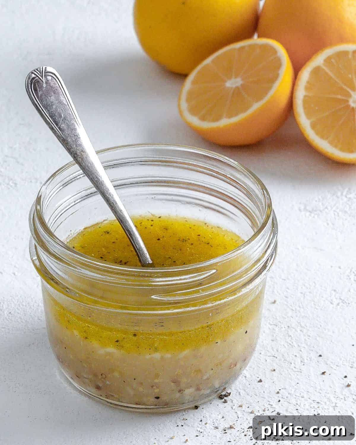 completed lemon dressing in a glass jar with a spoon in it and ingredients in the white background