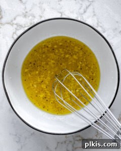 process of whisking lemon dressing ingredients together in white bowl against white background