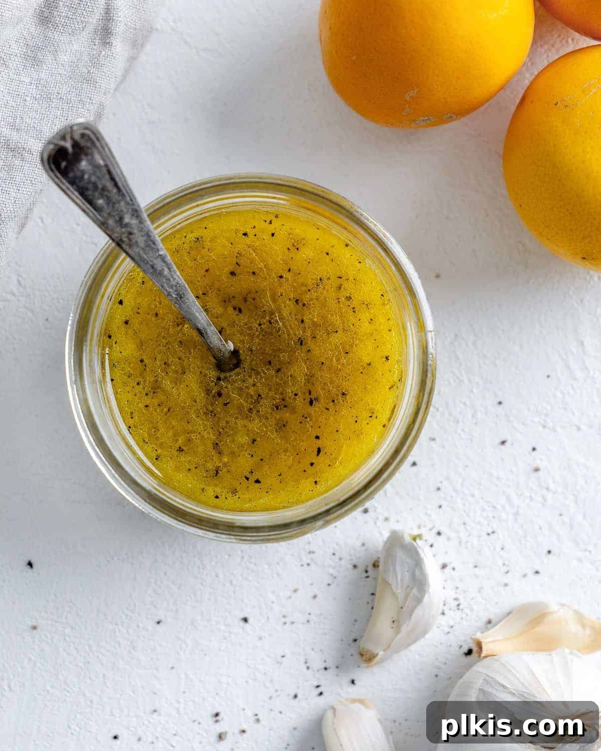 completed lemon dressing in a glass jar with a spoon in it and ingredients in the white background