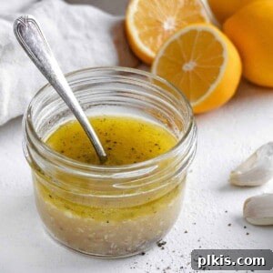 completed lemon dressing in a glass jar with a spoon in it and ingredients in the white background