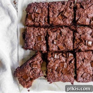 completed vegan Super Fudgy Brownies with a piece cut out on parchment paper