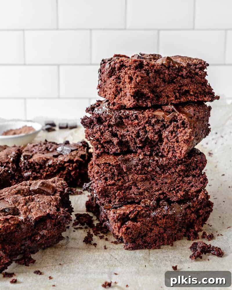 Heavenly Vegan Brownies 9 completed Super Fudgy Brownies stacked on each other in squares on parchment paper, perfectly sliced