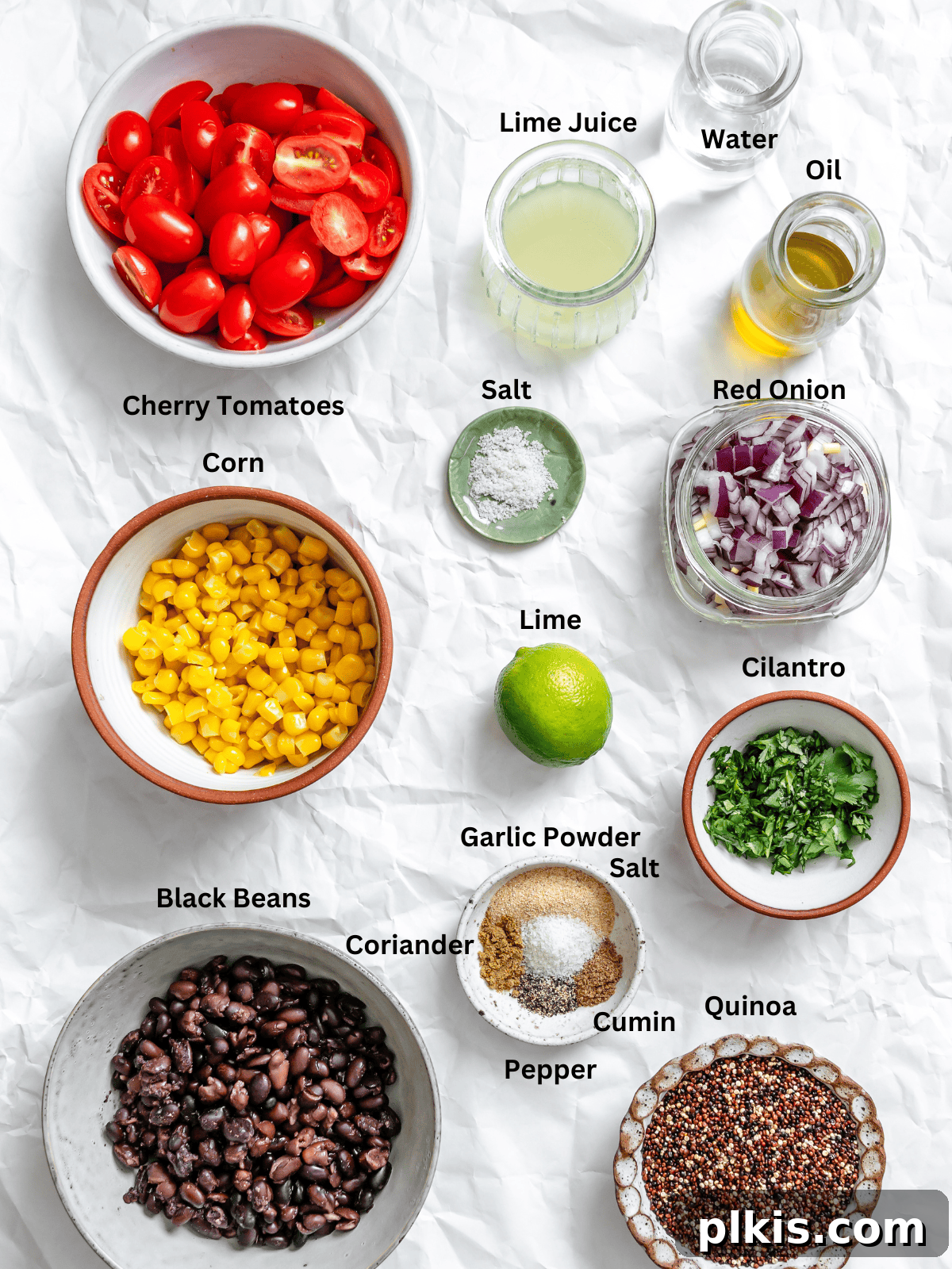 Southwestern Quinoa and Black Bean Fiesta 3 Ingredients for Black Bean Quinoa Salad measured out on a white surface, including quinoa, black beans, corn, red onion, cherry tomatoes, cilantro, and limes.