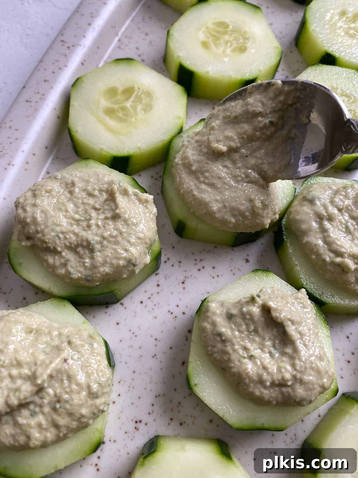 Refreshing Cucumber & Chive Sunflower Cream Bites 7 Process shot of adding sunflower seed mixture onto cucumber slices arranged on a platter.
