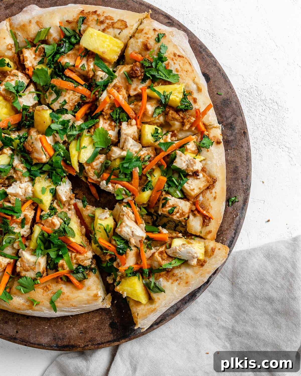 Irresistible Vegan Thai Pizza 10 completed shot of Thai pizza post being baked on brown and white surface with a slice cut out
