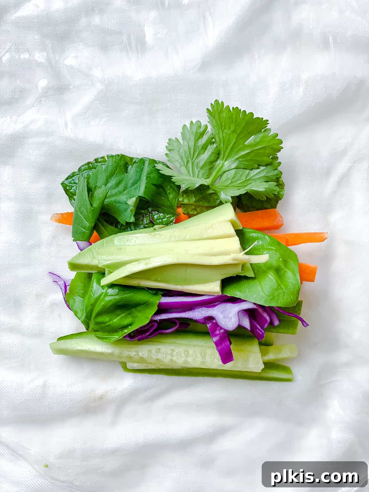 Vibrant Rainbow Rolls with Creamy Almond Shallot Dip 5 Close-up of neatly sliced fresh vegetables including carrots, cucumbers, and red cabbage, arranged on a white surface, ready for making Fresh Rainbow Rolls.