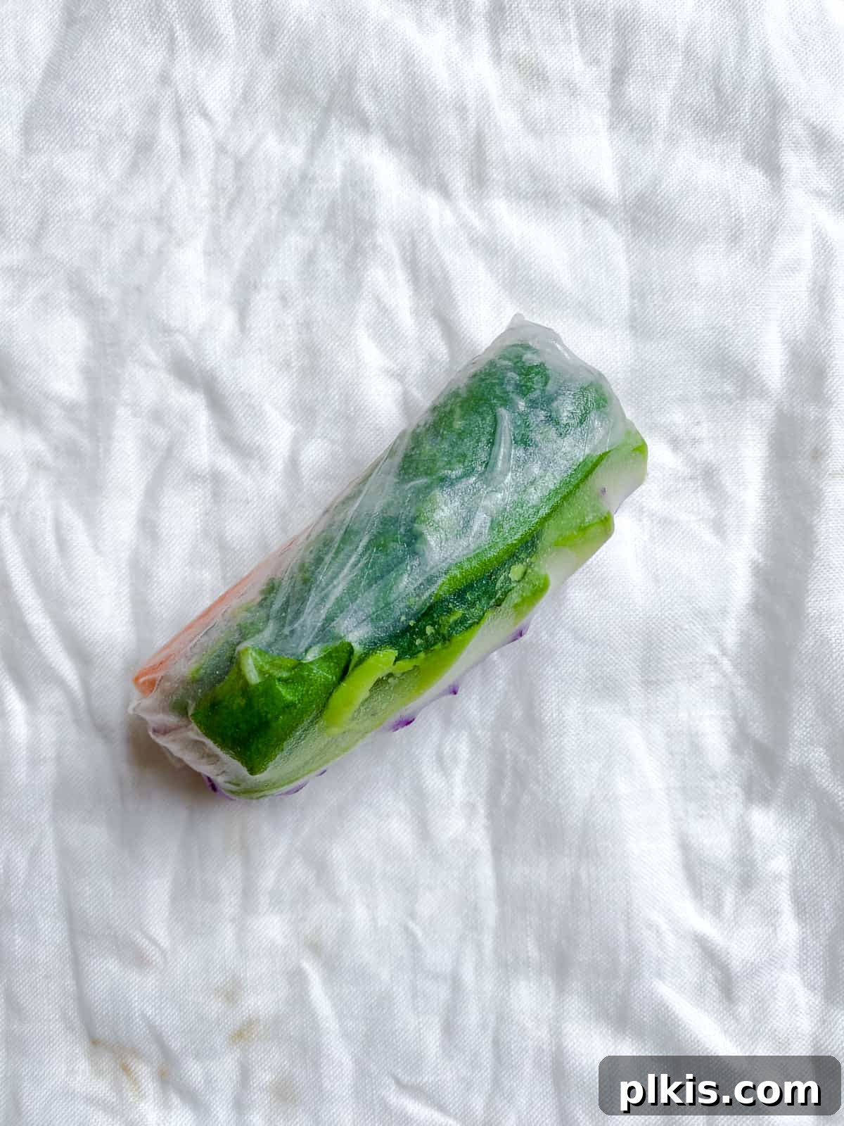 Vibrant Rainbow Rolls with Creamy Almond Shallot Dip 6 A freshly rolled, perfectly cylindrical rainbow roll resting on a white surface, showcasing the translucent rice paper wrapper and colorful filling.