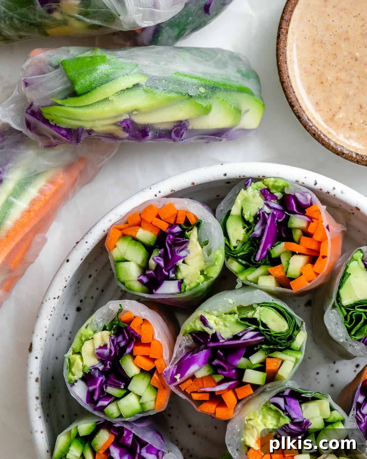 Vibrant Rainbow Rolls with Creamy Almond Shallot Dip 10 A bowl filled with several beautifully arranged Fresh Rainbow Rolls with Almond Shallot Sauce, garnished with fresh herbs, ready to be enjoyed.