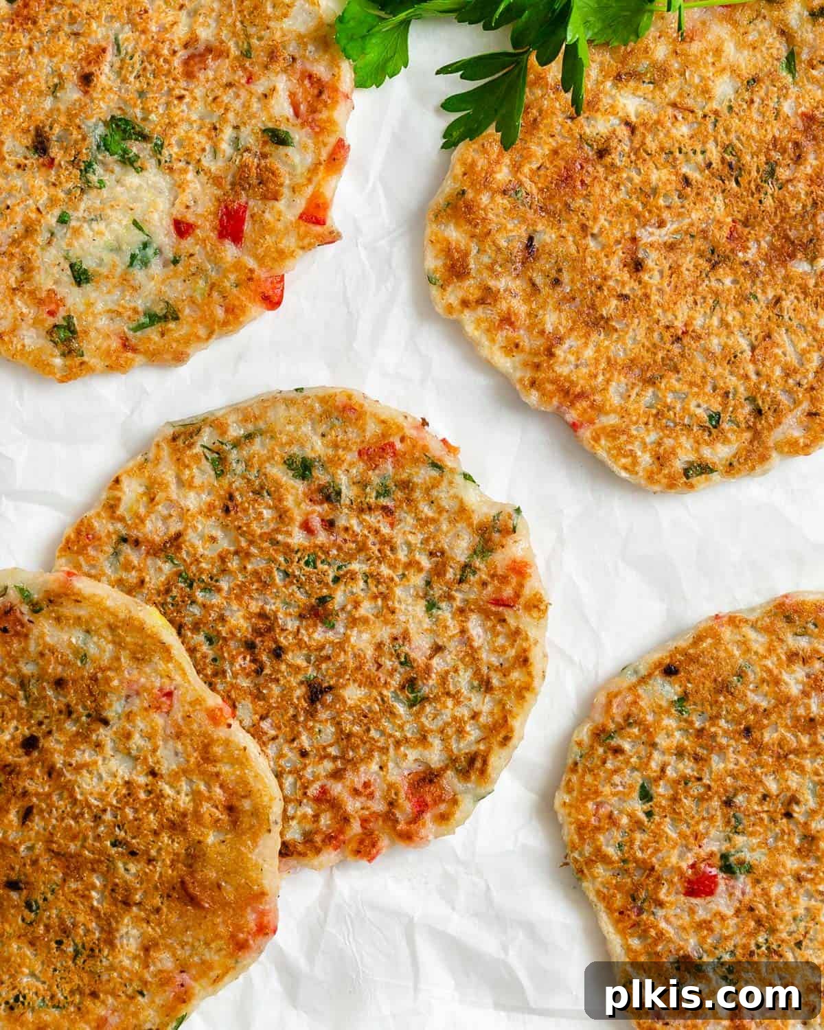 Crispy Vegan Potato Pancakes 11 A stack of perfectly cooked vegan potato pancakes, golden brown and garnished with fresh parsley, presented beautifully on a white surface.