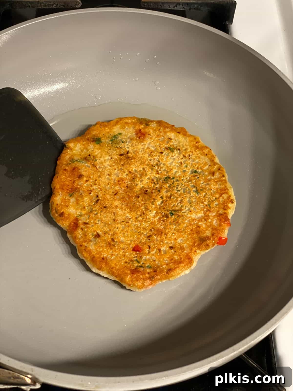 Crispy Vegan Potato Pancakes 10 A vegan potato pancake, perfectly golden brown on one side, has just been flipped in a hot skillet, ready to cook the other side.