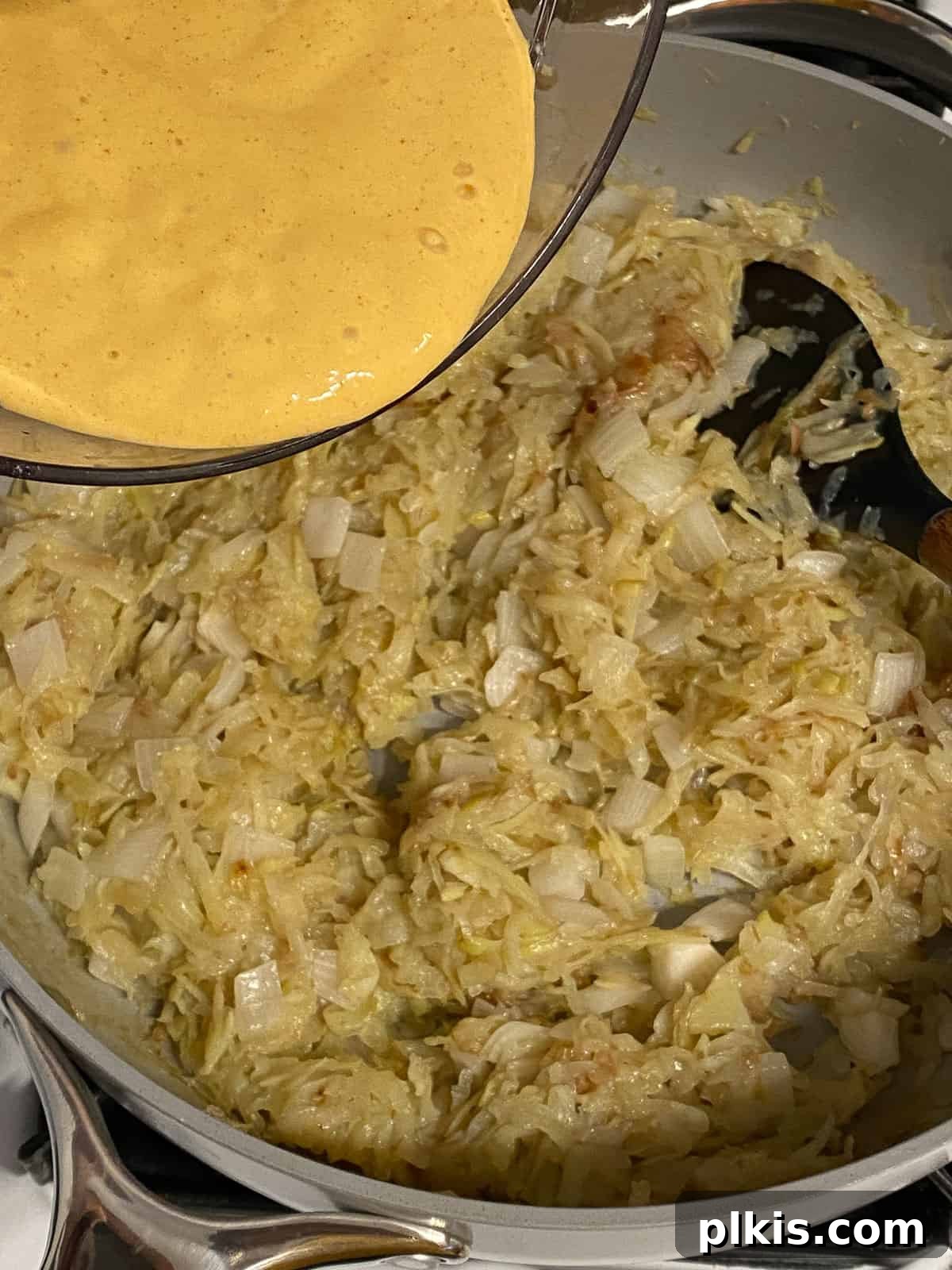 Process shot of adding blended tofu mixture to the potato and onion mixture in a pan, combining the frittata base with the filling.