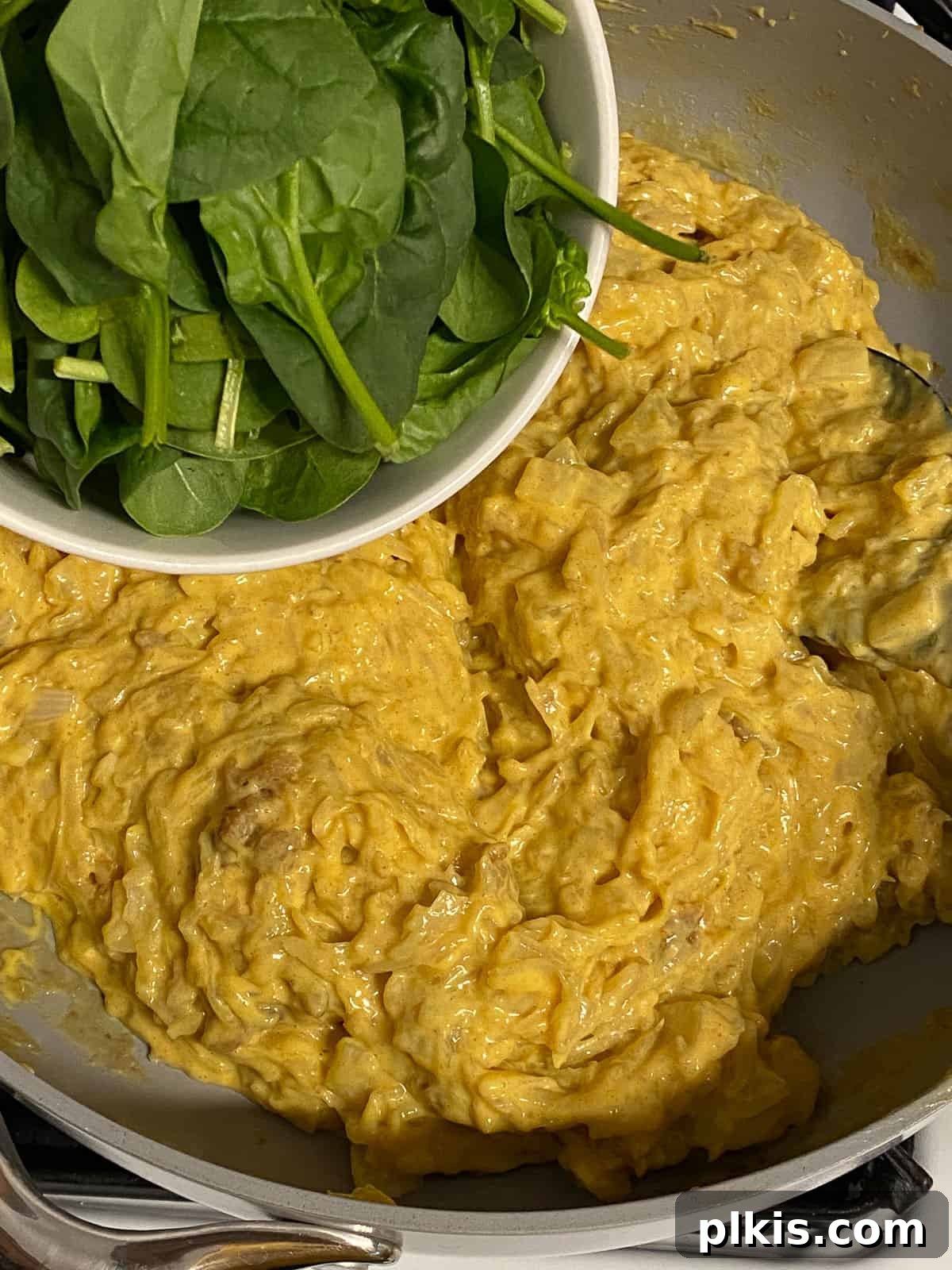Process shot of adding spinach to a pan, incorporating fresh greens into the vegan potato frittata mixture.