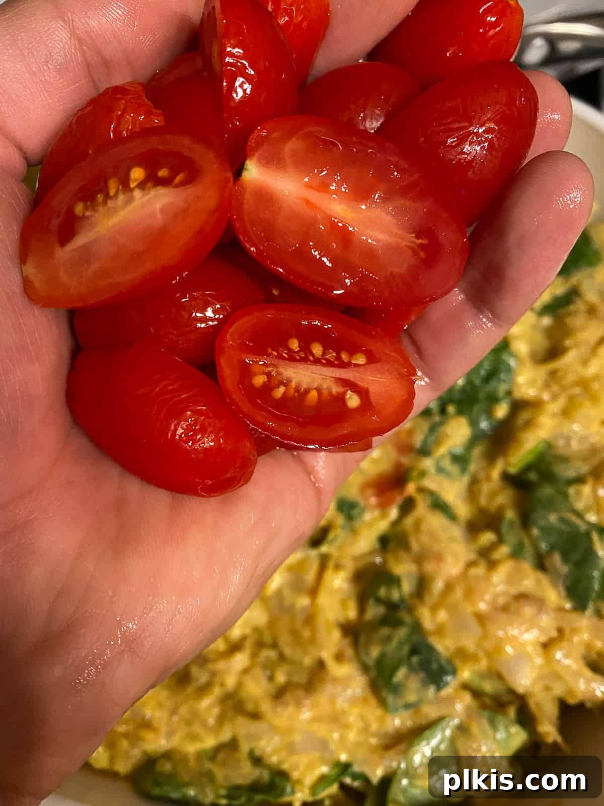 Process shot of adding tomatoes to a pan, topping the vegan frittata mixture with fresh, colorful tomato slices.