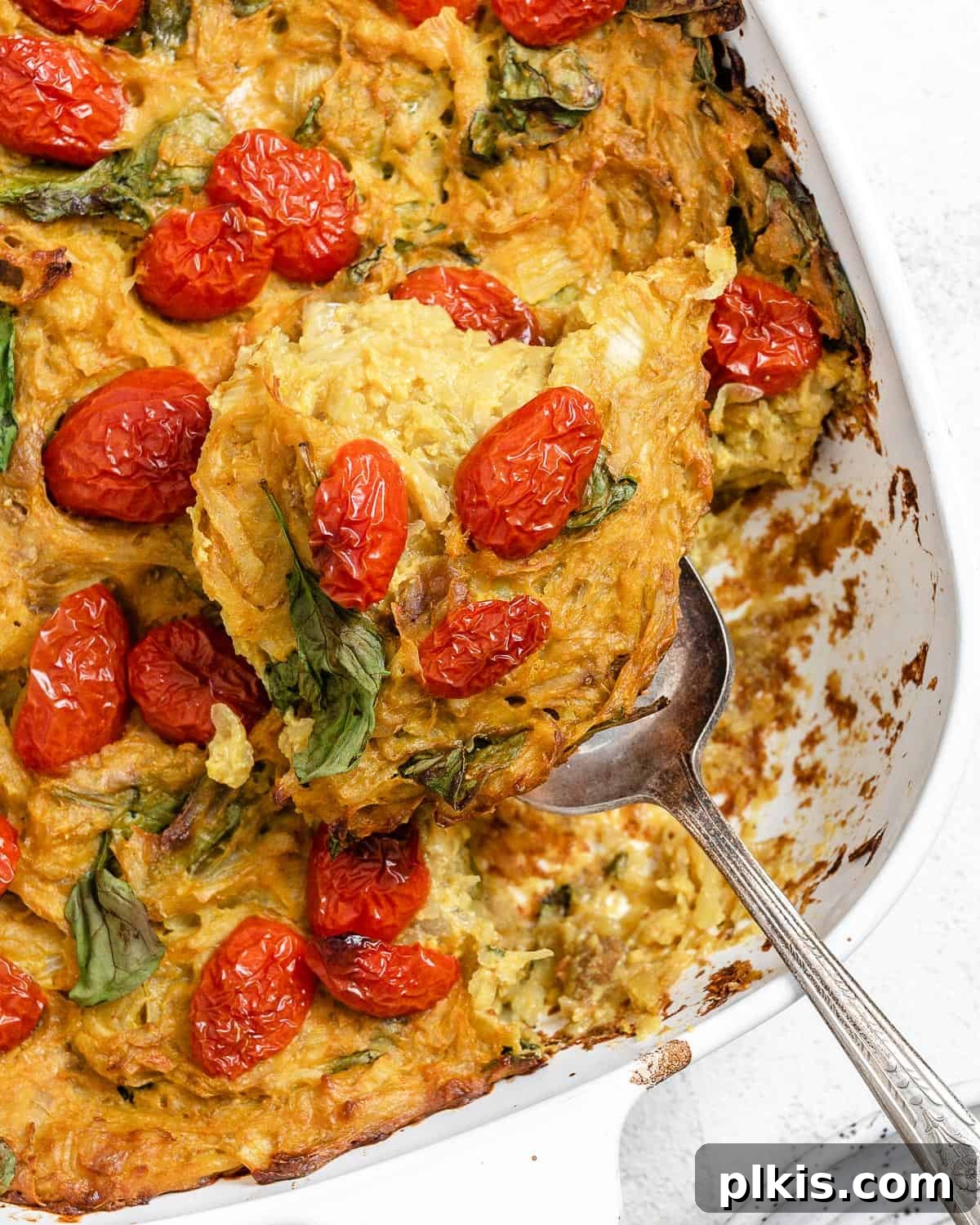 Completed Vegan Potato Frittata [Breakfast Casserole] in a baking tray with a spoonful being scooped out, against a light background, highlighting its appealing texture and rich fillings.