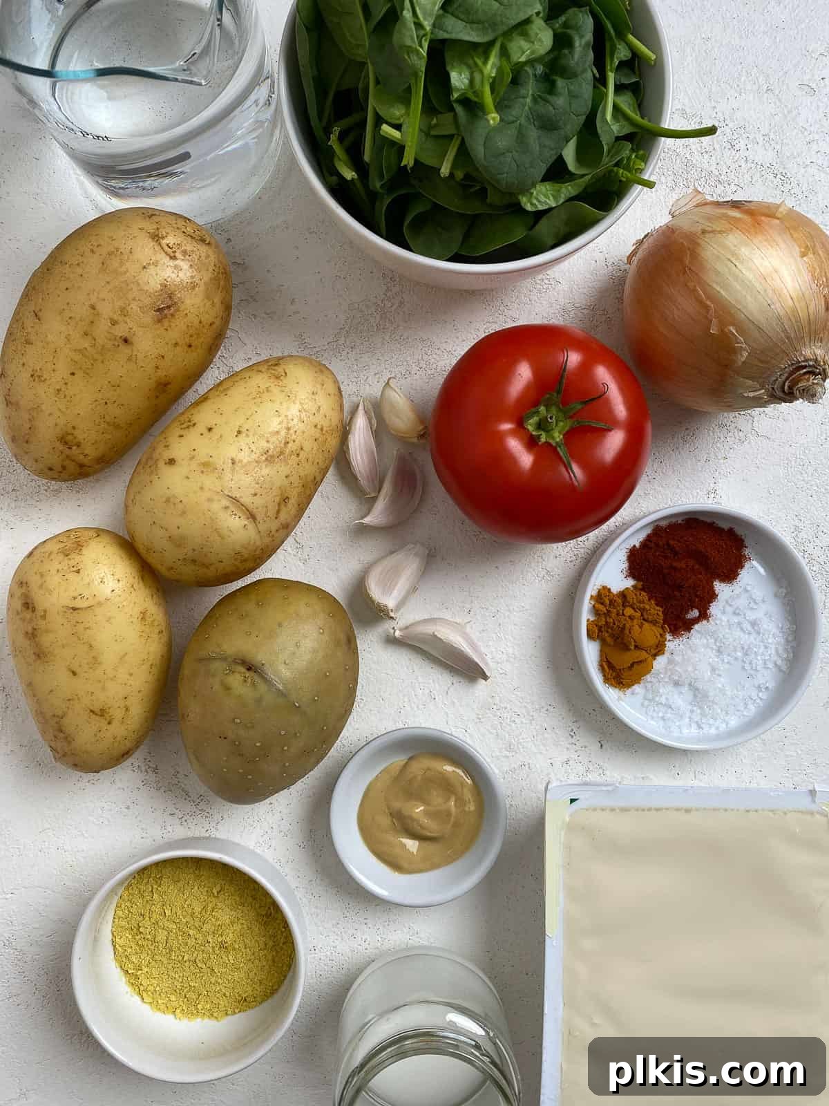Ingredients for Vegan Potato Frittata [Breakfast Casserole] laid out on a white background, including potatoes, tofu, onions, garlic, and spices.