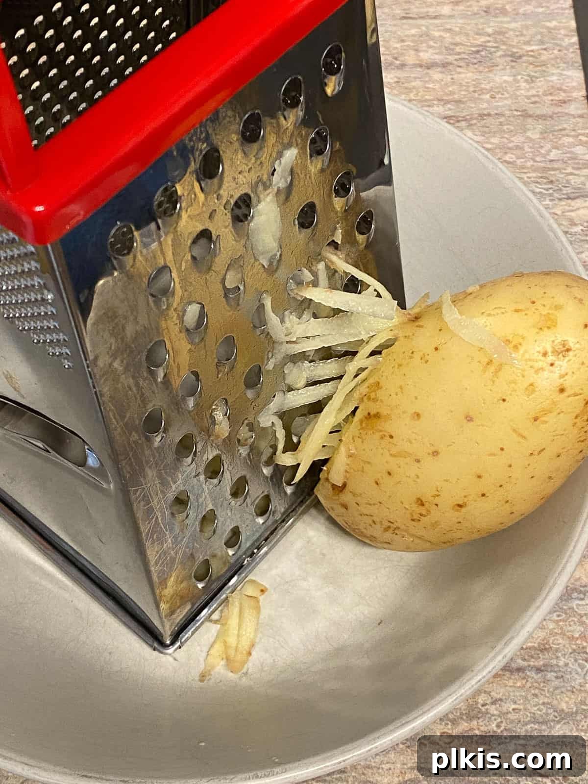 Process shot of shredding potatoes with a grater into a bowl, demonstrating the initial preparation step for the vegan frittata.