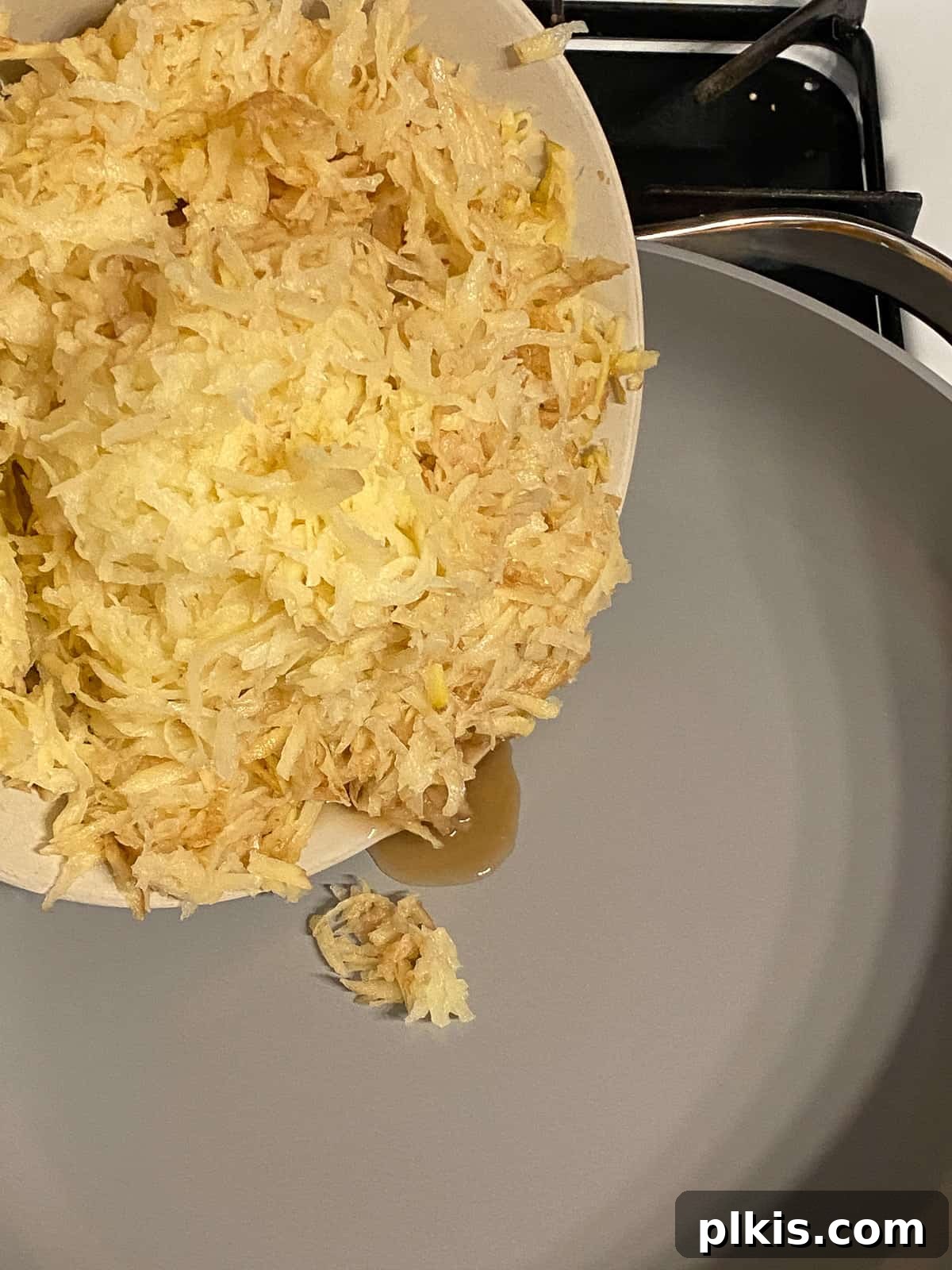 Process shot of adding shredded potatoes to a pan, illustrating the step of preparing the potato base for the frittata.