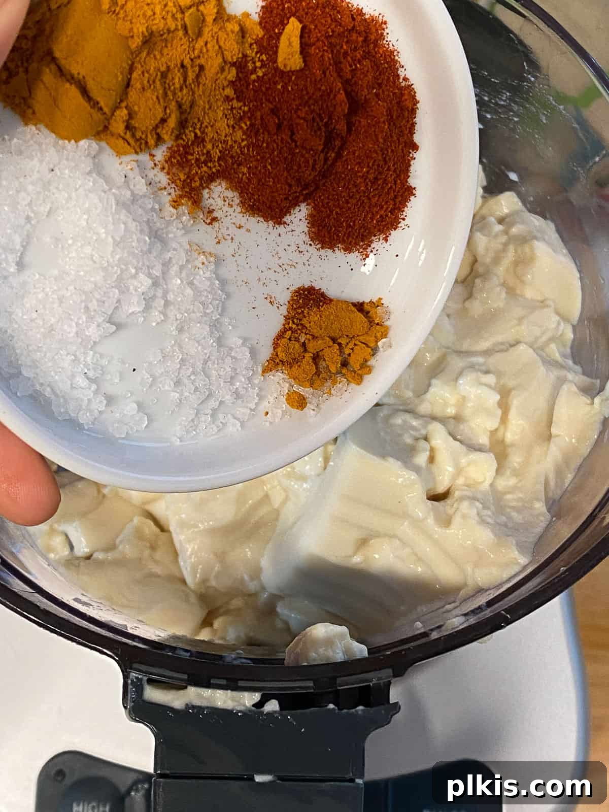 Process shot of adding various spices to a blender, preparing the flavor base for the vegan tofu frittata.