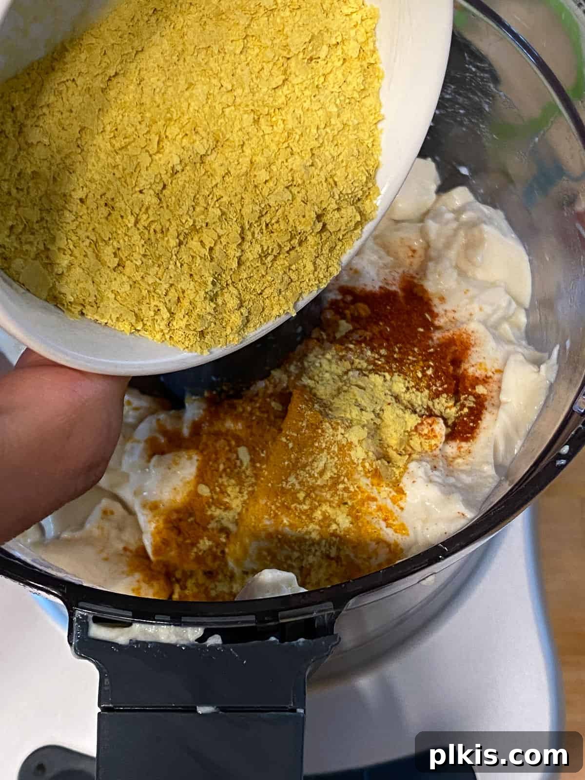 Process shot of adding nutritional yeast to a blender, a key ingredient for the umami and 'cheesy' flavor in the vegan frittata.