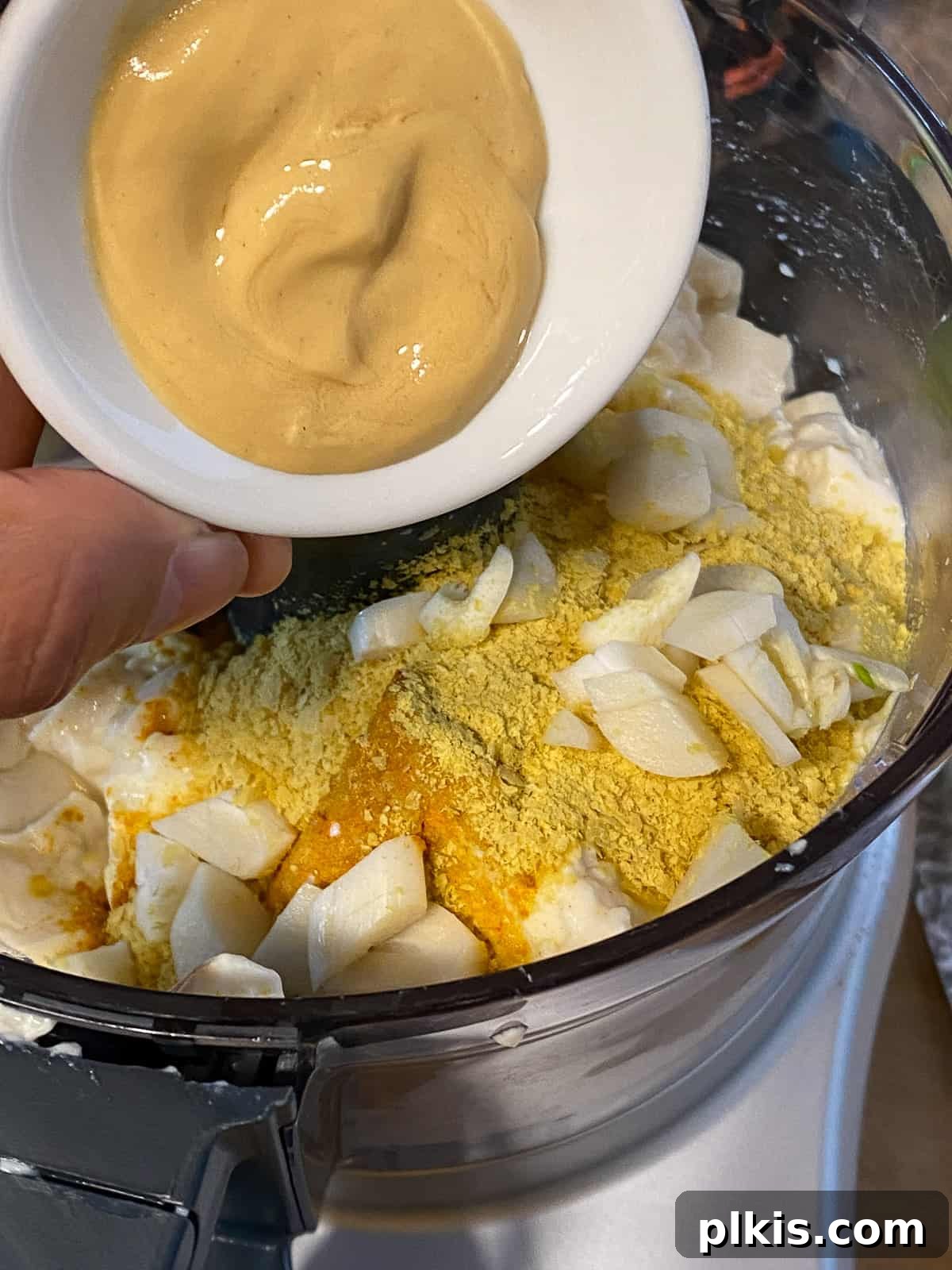 Process shot of adding Dijon mustard to a blender, an ingredient that enhances the depth and color of the vegan frittata.
