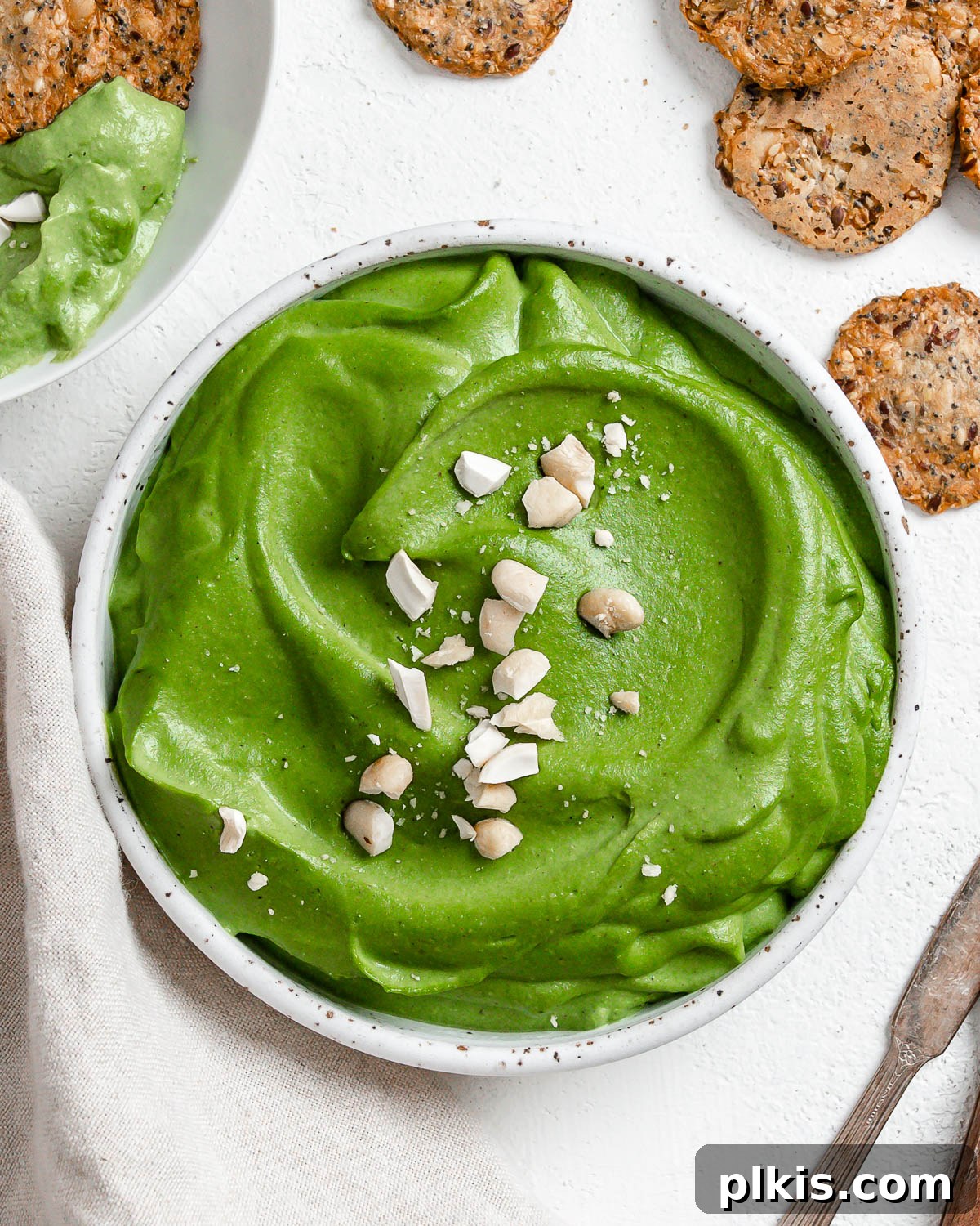Dreamy Vegan Spinach Dip 2 A beautifully presented vegan spinach dip, rich green and creamy, garnished with fresh herbs and served with a variety of crispy crackers on a light background, inviting guests to dig in.
